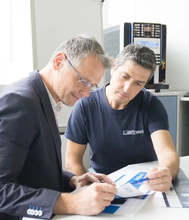Herbert Meyer and a colleague sit at a desk reviewing printed documents together in a brightly lit office setting.