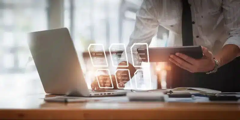 A person stands at a desk using a tablet and laptop, with digital data icons overlaid—representing business, data analysis, and efficient workflows powered by a document management system.