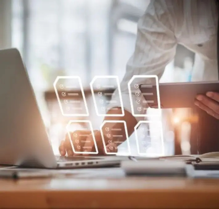 Person using a laptop and tablet at a desk with digital icons of documents and checklists superimposed, representing efficient digital workflow and Product Data Management.