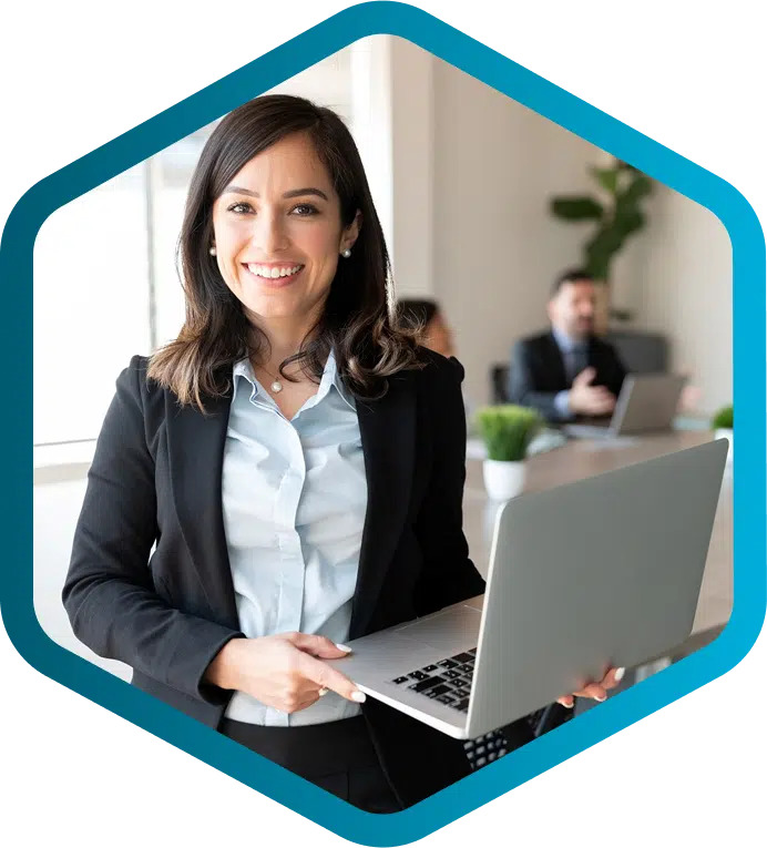 A woman in business attire holds a laptop and smiles at the camera in an office setting, embodying the efficiency of the digital thread as her colleagues collaborate in the background.