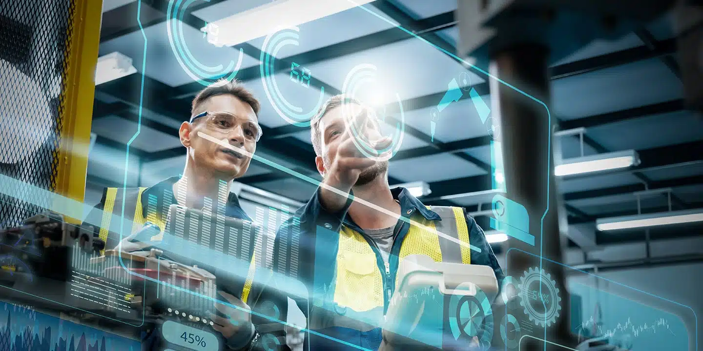 Zwei Arbeiter in Sicherheitswesten und Schutzbrillen bedienen in einer modernen Industrieumgebung Maschinen, die mit digitalen Daten und Schnittstellengrafiken überlagert sind.