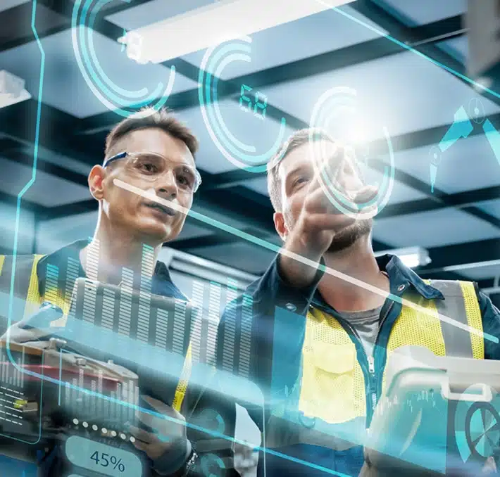 Two workers in safety vests inspect virtual data displays, with digital graphs and interface elements superimposed in a modern industrial setting.