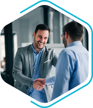 Two men in business attire shake hands and smile in a modern office setting, successfully finalizing an engineering change management agreement.