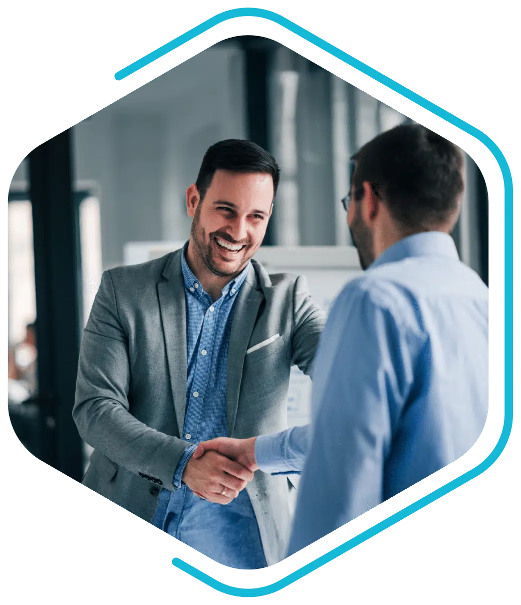 Two men in business attire shake hands and smile in an office setting, suggesting a professional or positive interaction.