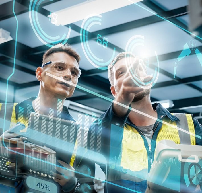 Two workers in safety vests inspect virtual data displays, with digital graphs and interface elements superimposed in a modern industrial setting.
